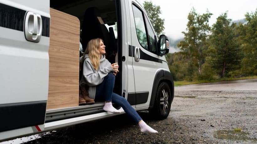 Eine Frau sitzt bei geöffneter Schiebetür in einem weißen Transporter mit einer Tasse in den Händen. Dieser Transporter steht über 57MOBIL zum Mieten zur Verfügung.