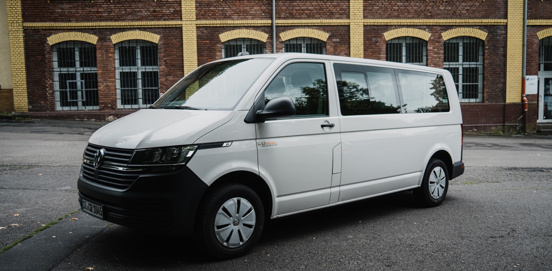 Ein weißer VW Transporter vor einem roten Backsteingebäude geparkt - ideal für vielseitige Transporte und zum Mieten.