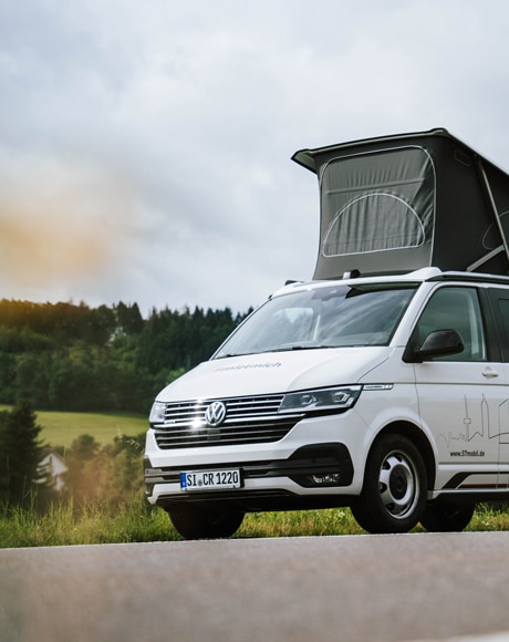 Weißer VW California mit praktischem Aufstelldach zum Mieten.