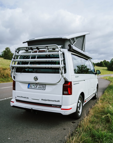 Heckansicht eines weißen VW Californias mit Gepäckträger - jetzt mieten und auf Tour gehen!